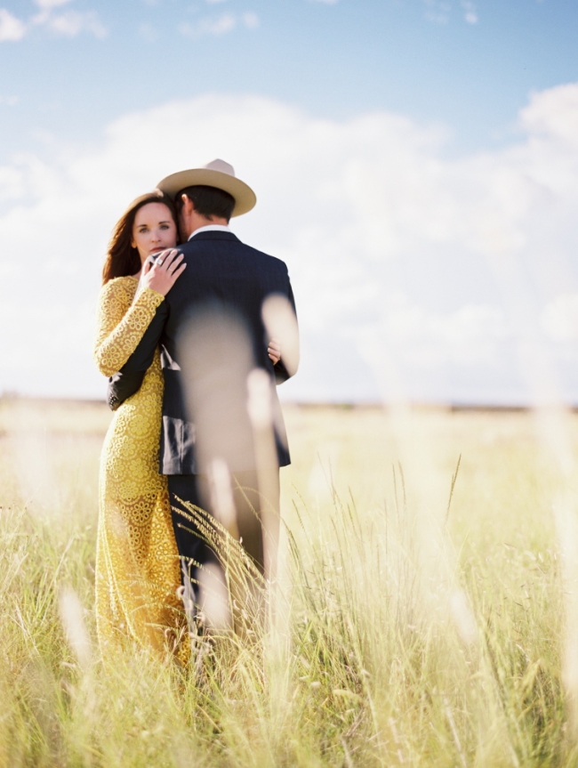 Woman in yellow dress embracing man in grey suit and stetson standing in tall grass