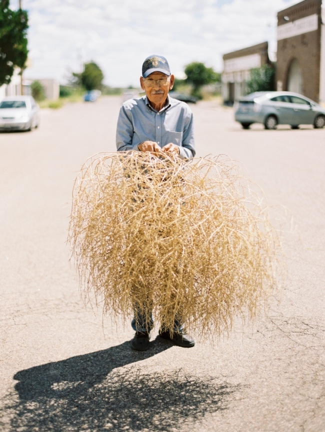 older hispanic man holding large tumbleweed in the middle of Marfa Texas street