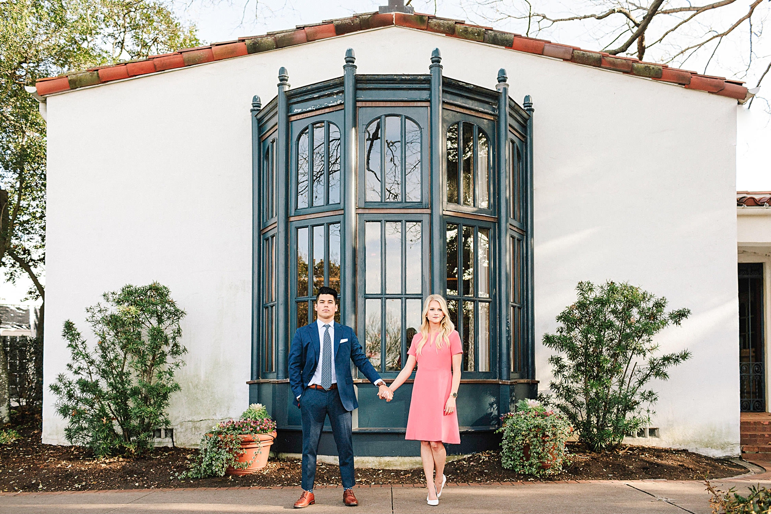man in blue suite holding hands with woman in pink dress standing in front of Spanish building