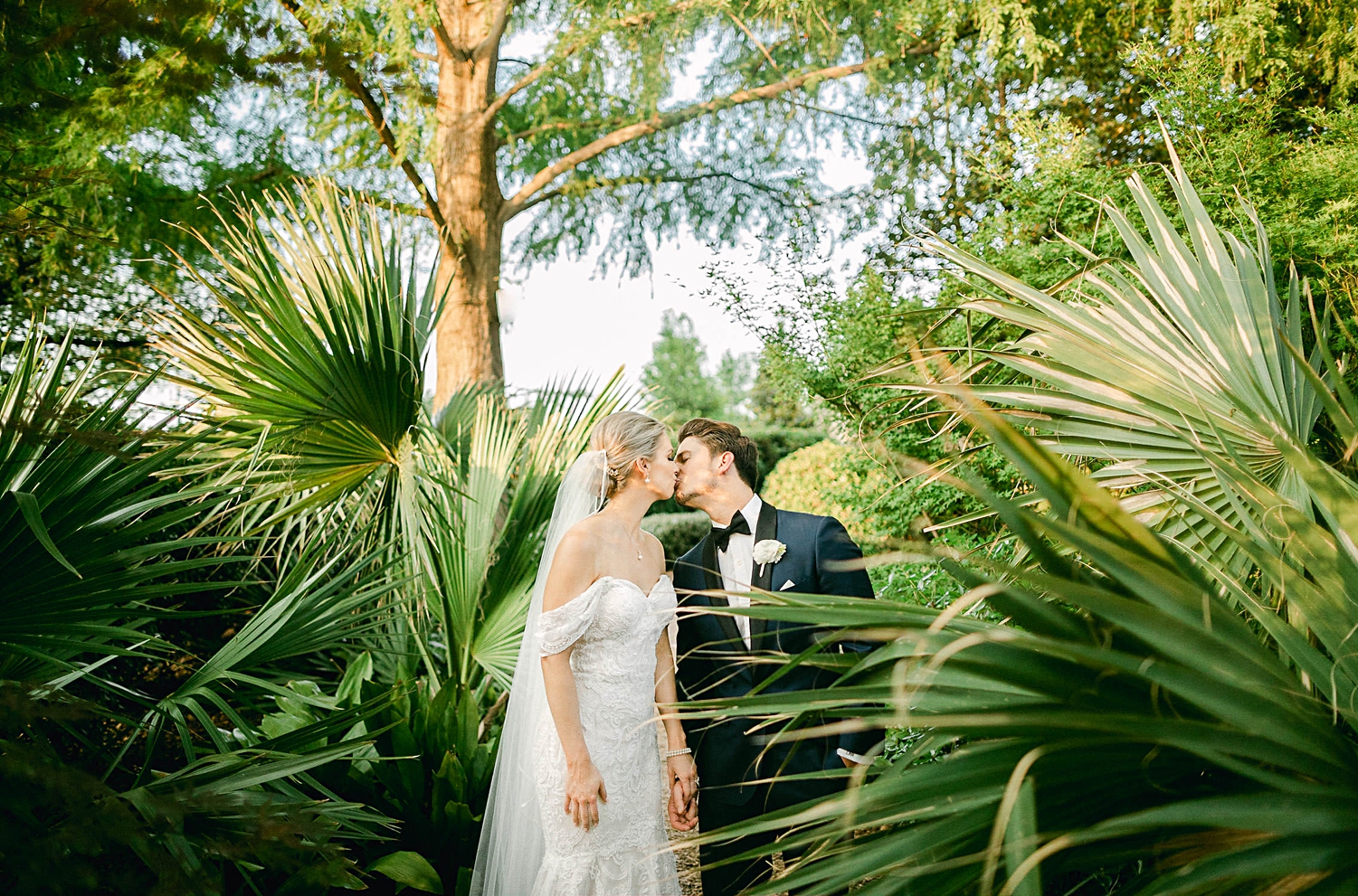 Bride and groom kissing in front of green palm leaves wedding