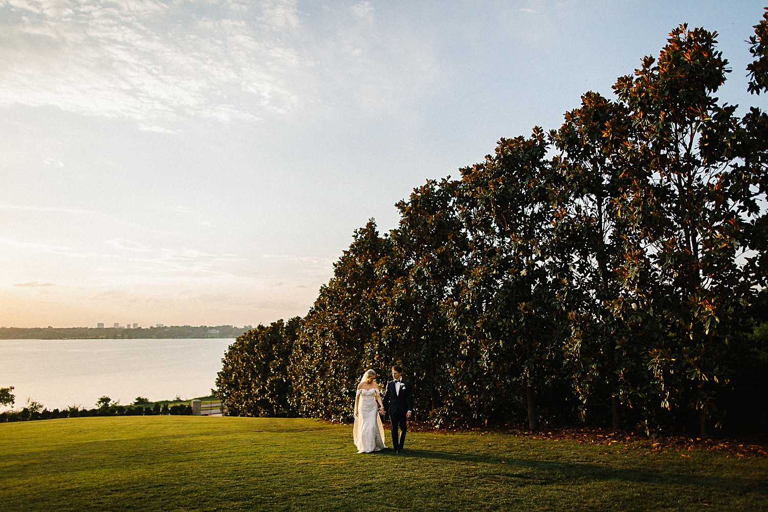bride and groom walking together in front of trees lake blue sky Dallas arboretum Venue 