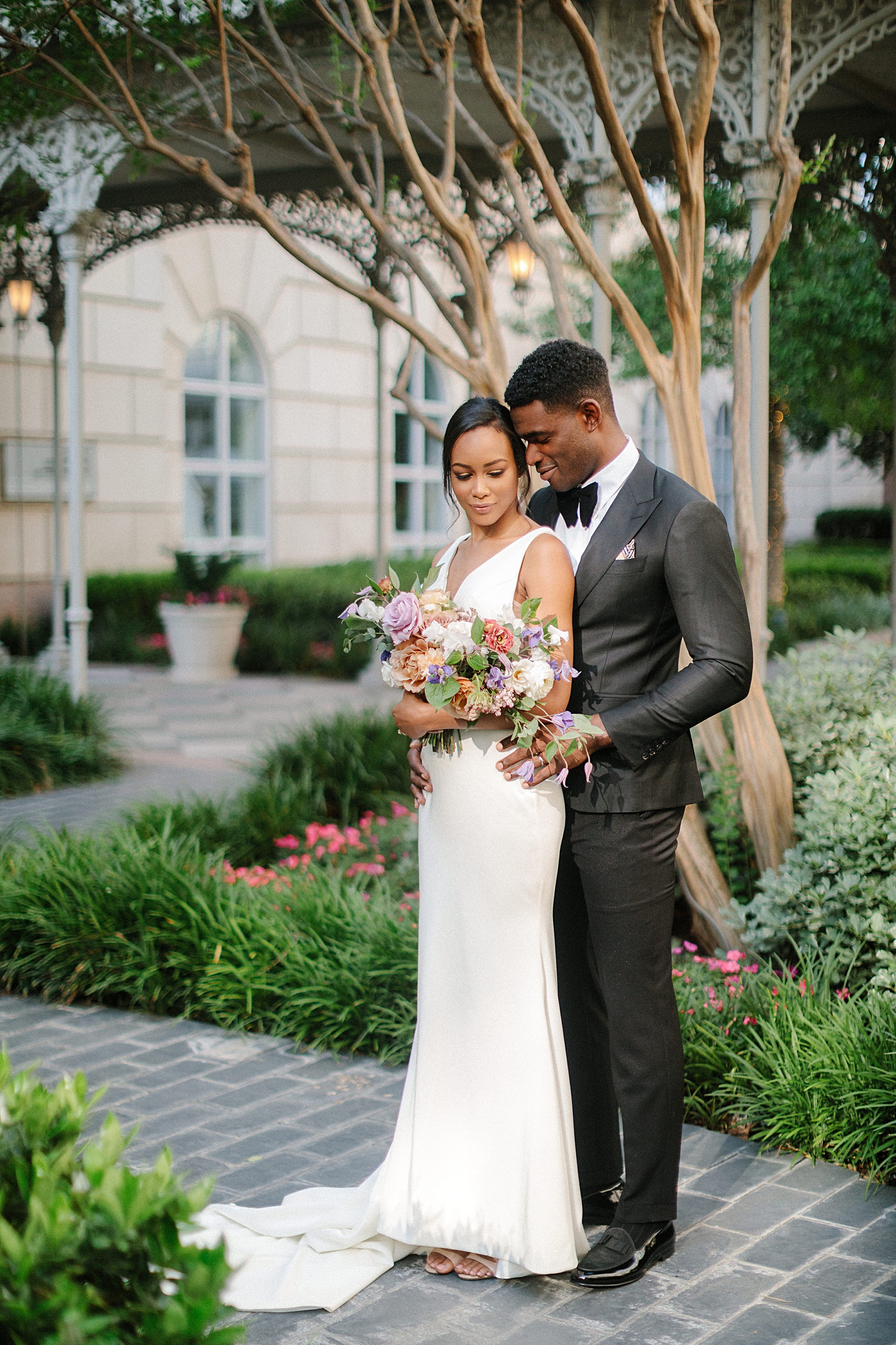groom in black tuxedo holding bride in modern wedding dress french garden