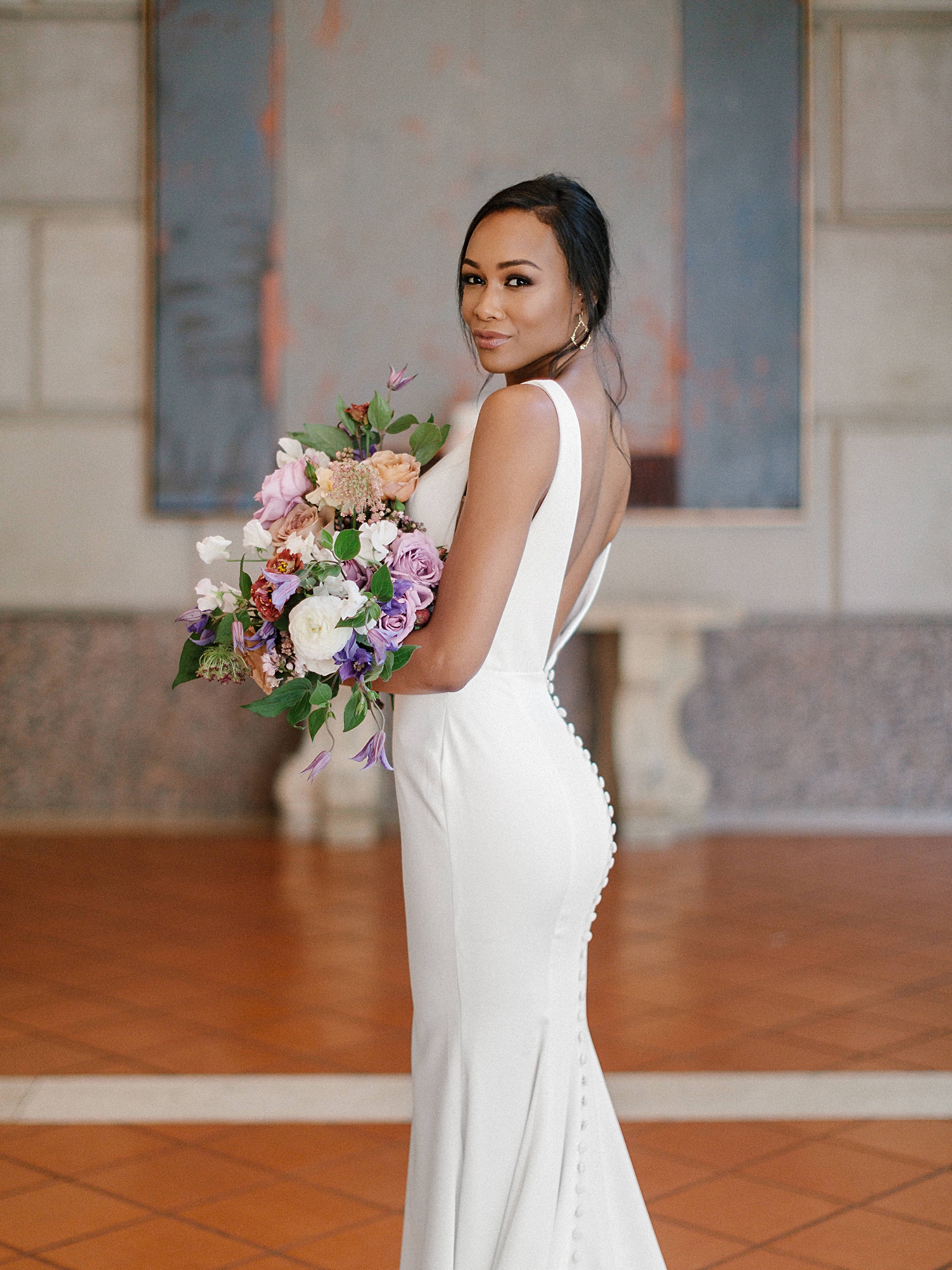 Bride in modern wedding dress holding colorful bouquet in white stone french room