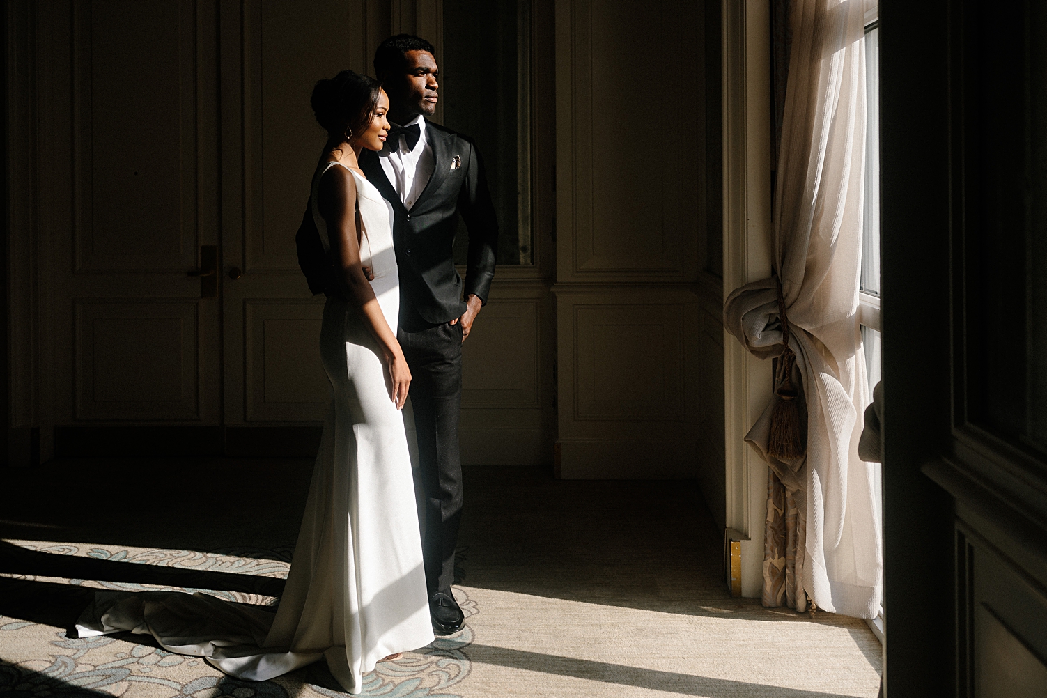 Black bride and groom standing together in front of window