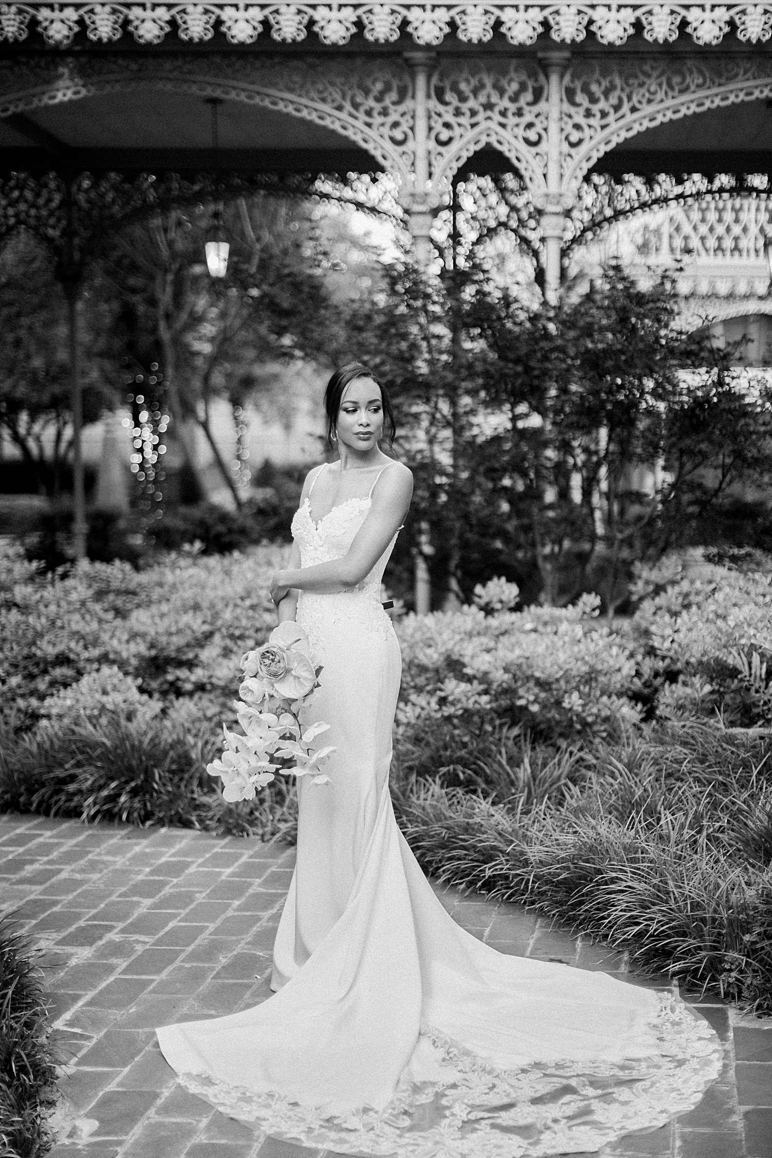 Black and white bride in long wedding dress and bouquet standing in crescent hotel garden