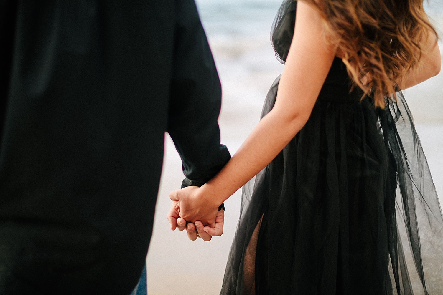 couple in black holding hands at beach