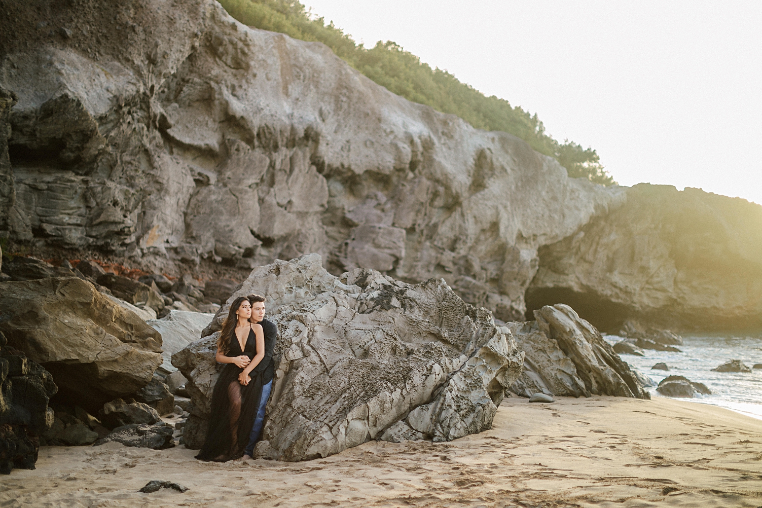 couple on beach black dress tule leaning on rock
