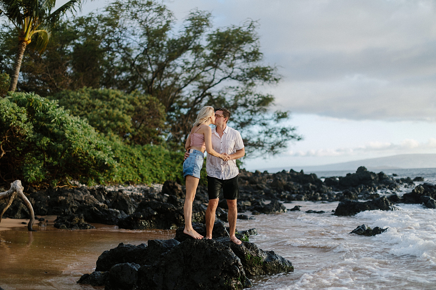 girl kissing man standing on black rock on beach hawaii