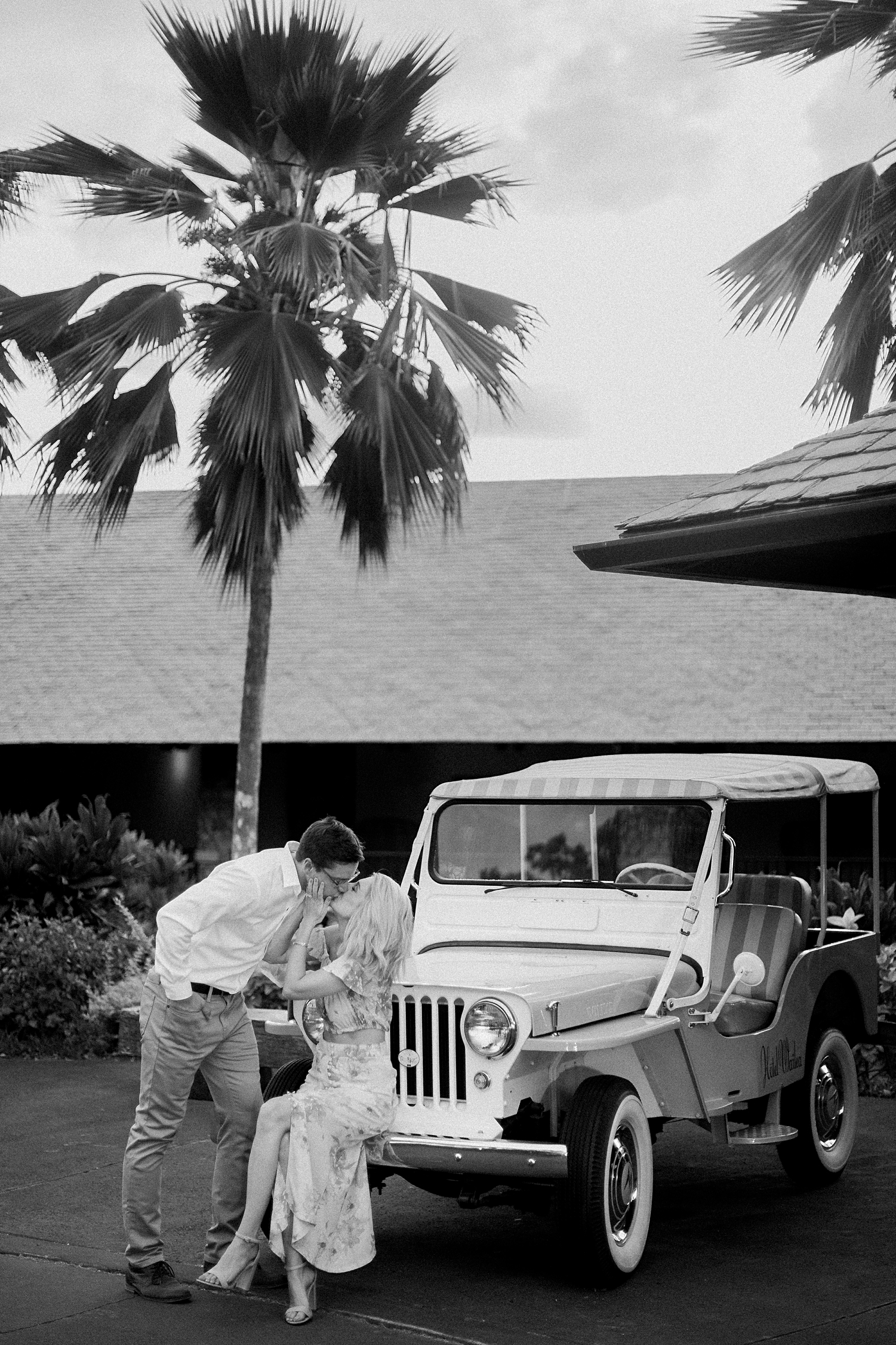 husband kissing wife by vintage Jeep at Hotel Wailea in Maui black and white