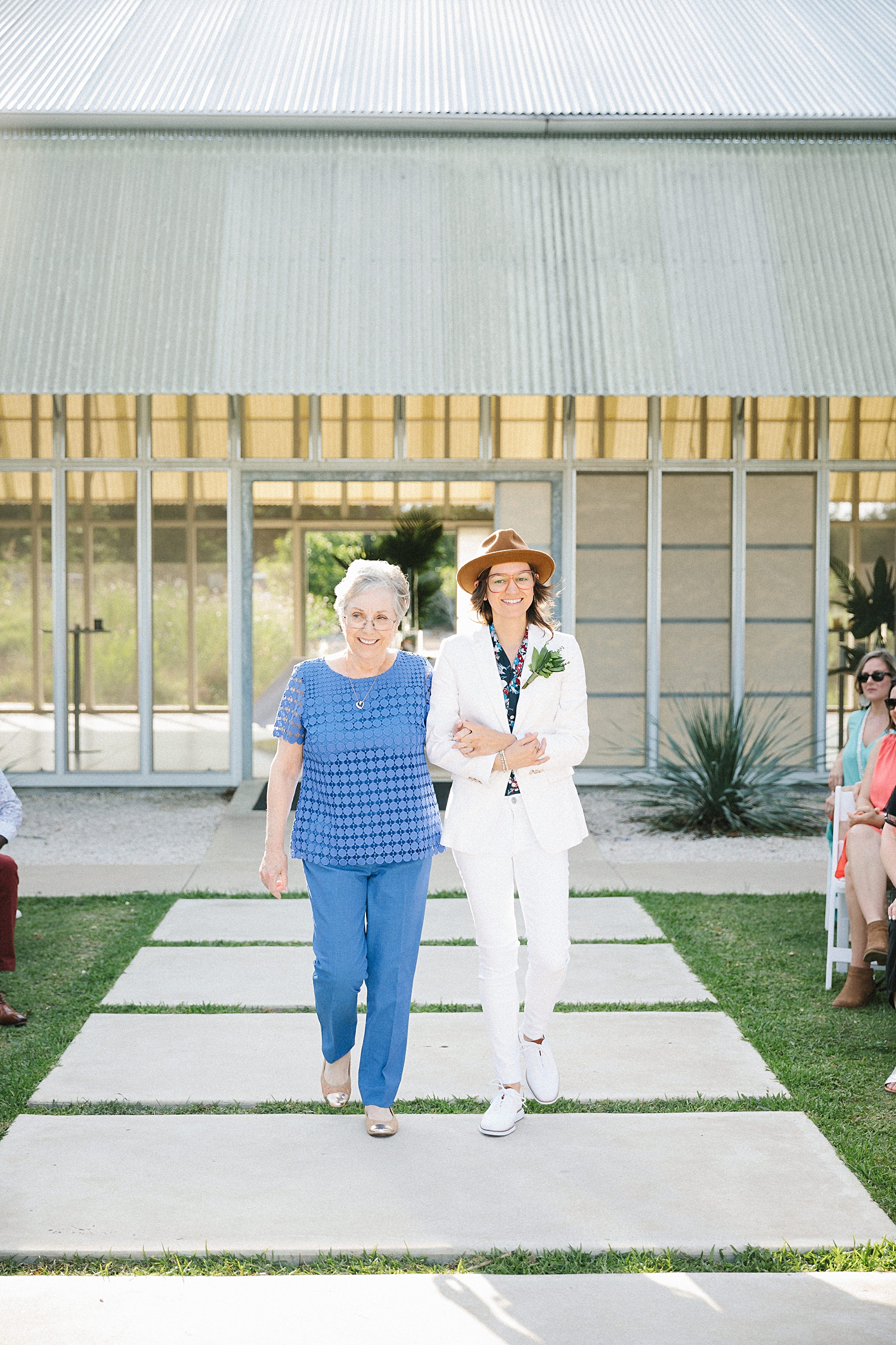 bride in white suit walking down aisle with grandmother