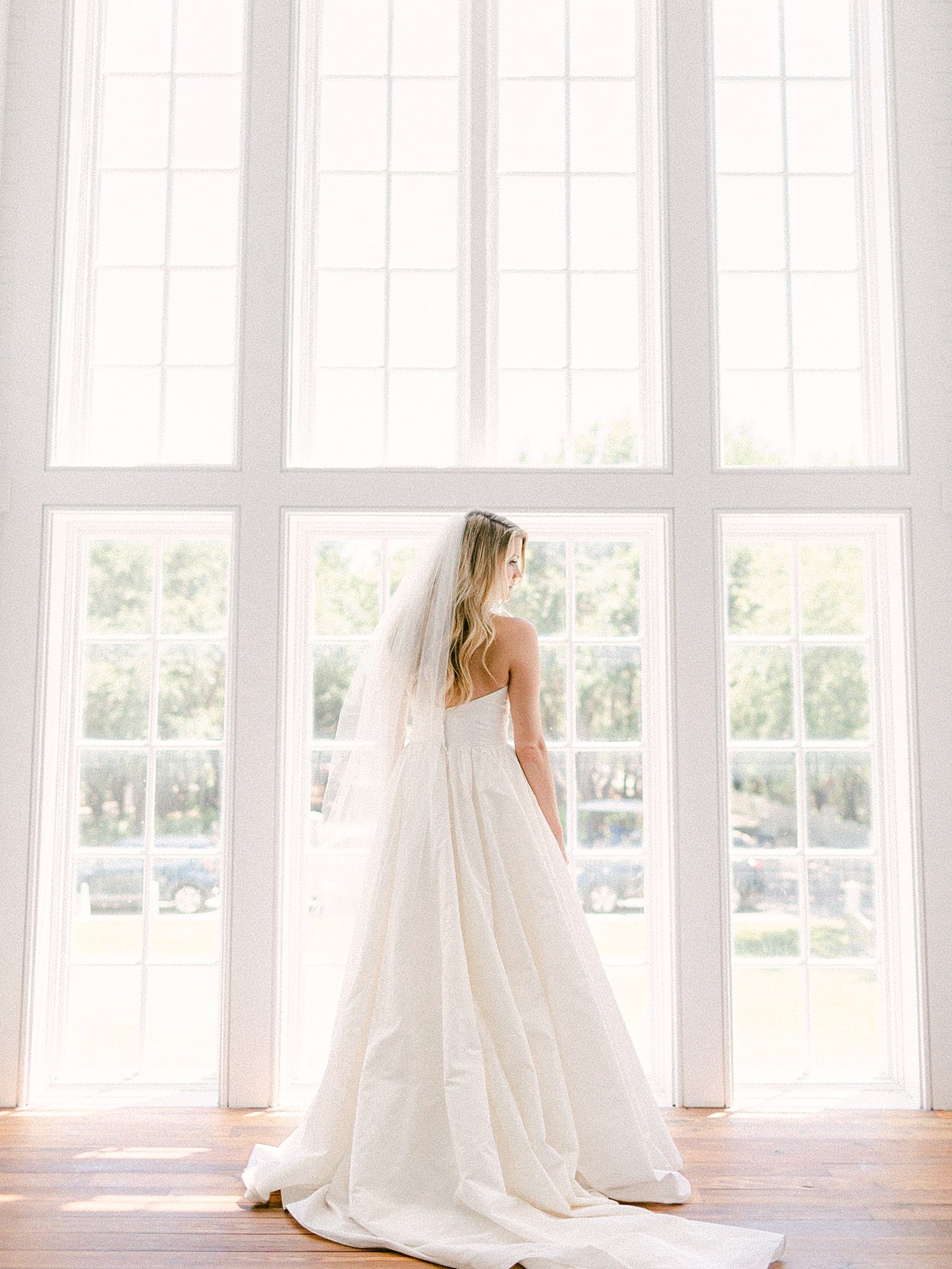 Bride in white wedding dress standing in front of large windows Seaside Chapel Florida