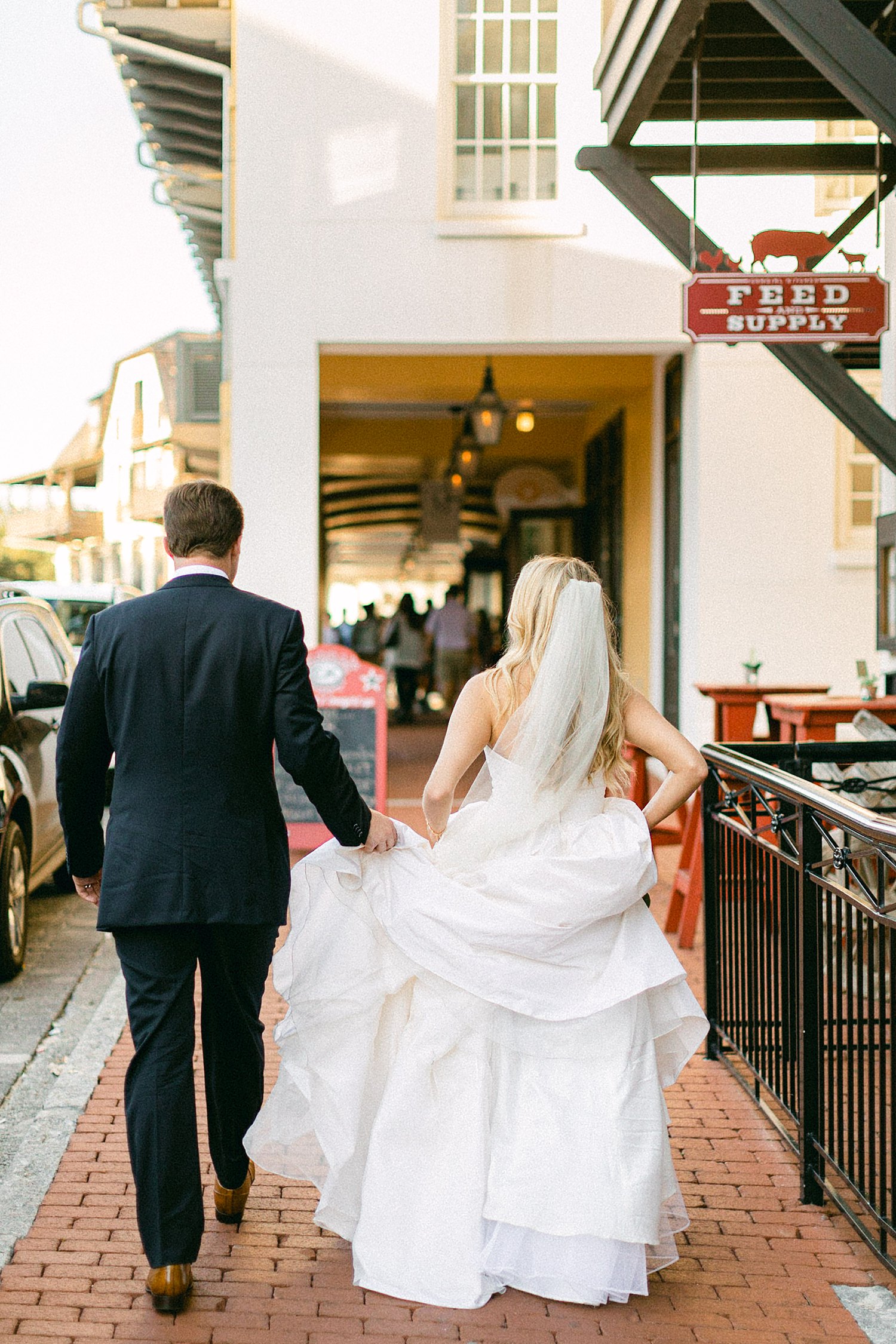 Groom holding brides dress while walking down street in Rosemary Beach Florida at Pearl Hotel Wedding