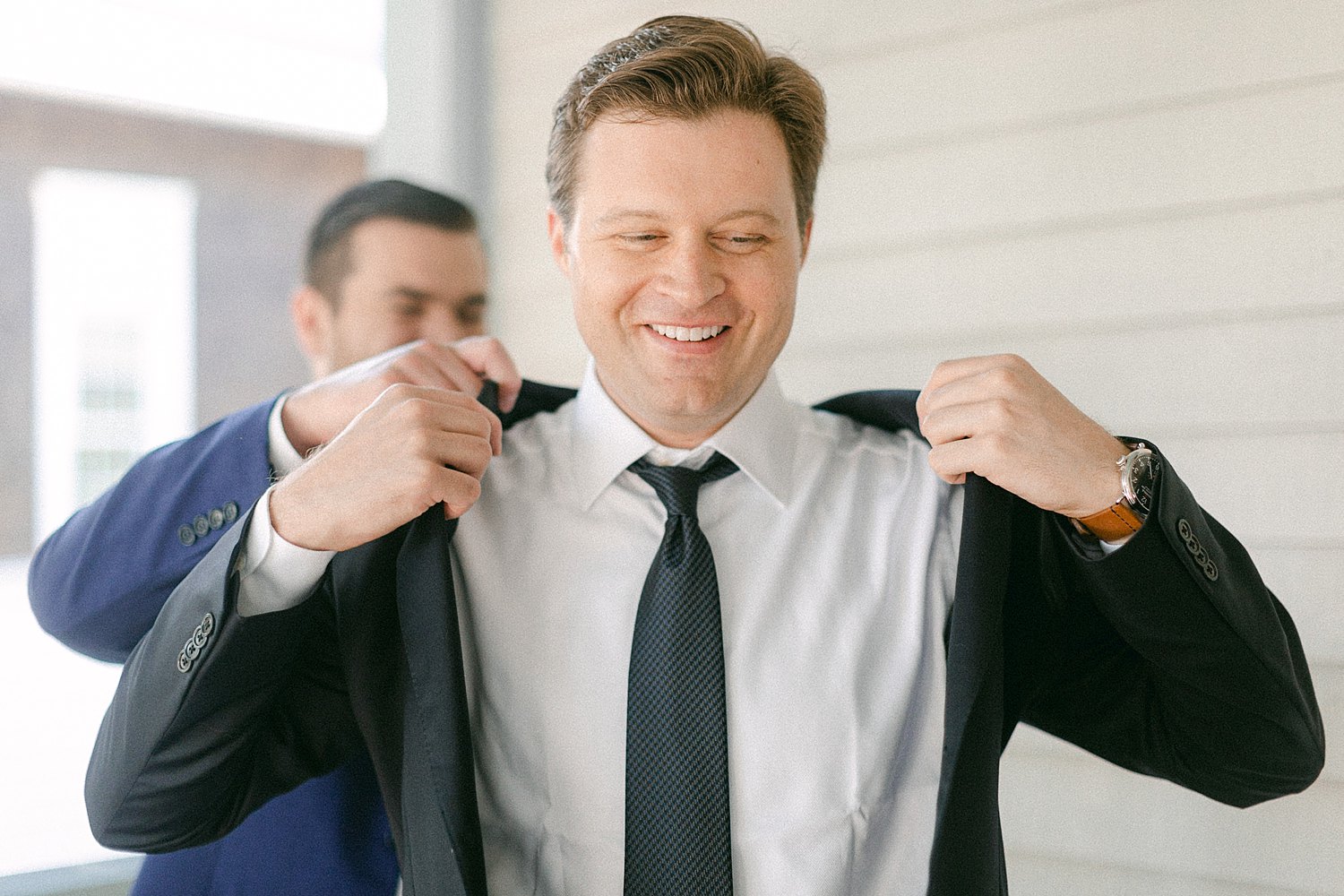 brother helping groom put on suit jacket smiling