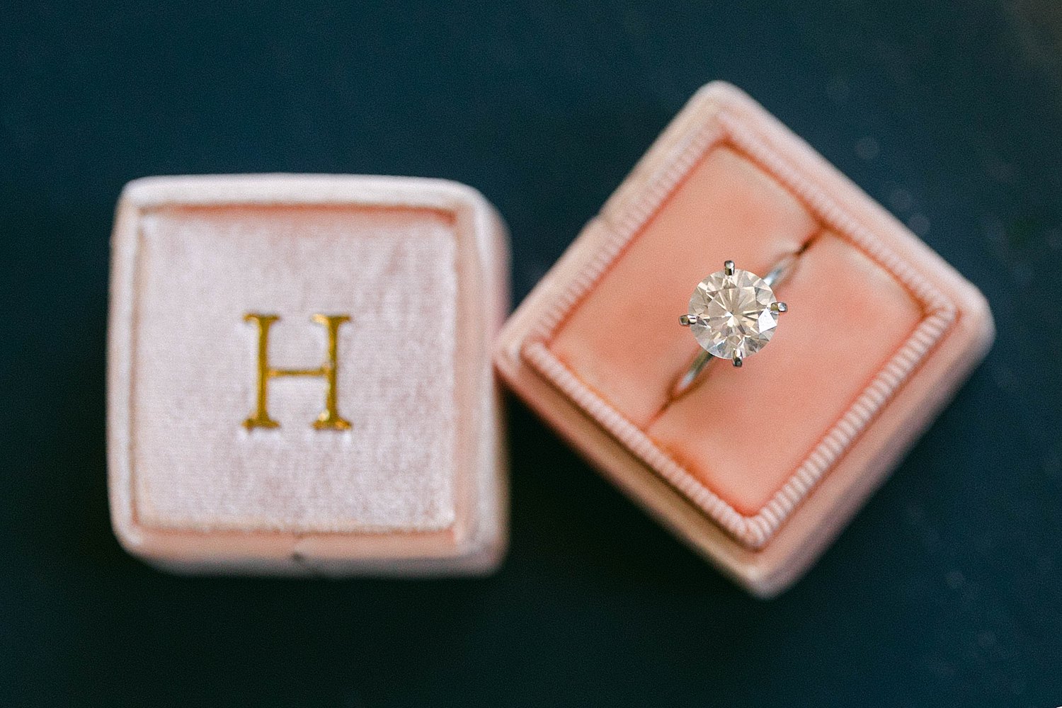 Diamond ring with gold band sitting in pink ring box with H on top