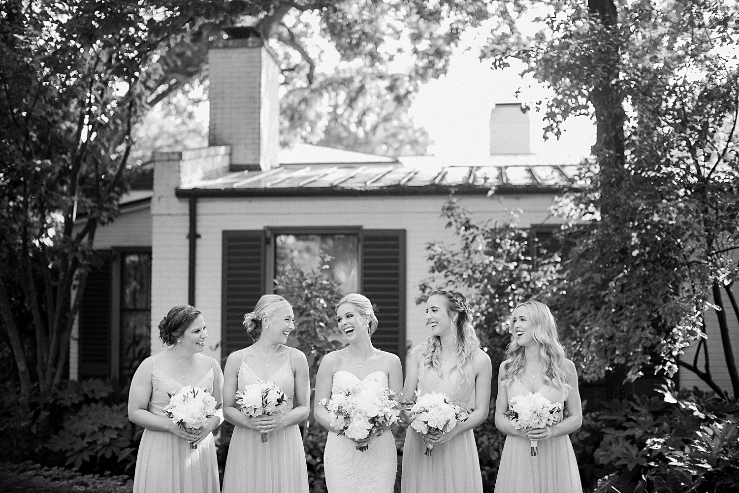 Bride holding white bouquet laughing with four bridesmaids at Dallas Arboretum Wedding