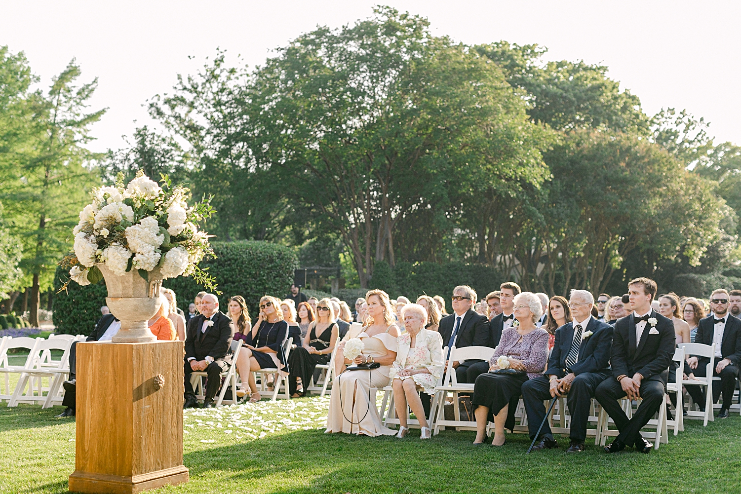 Dallas Arboretum wedding ceremony guests sitting in white chairs in front of green trees