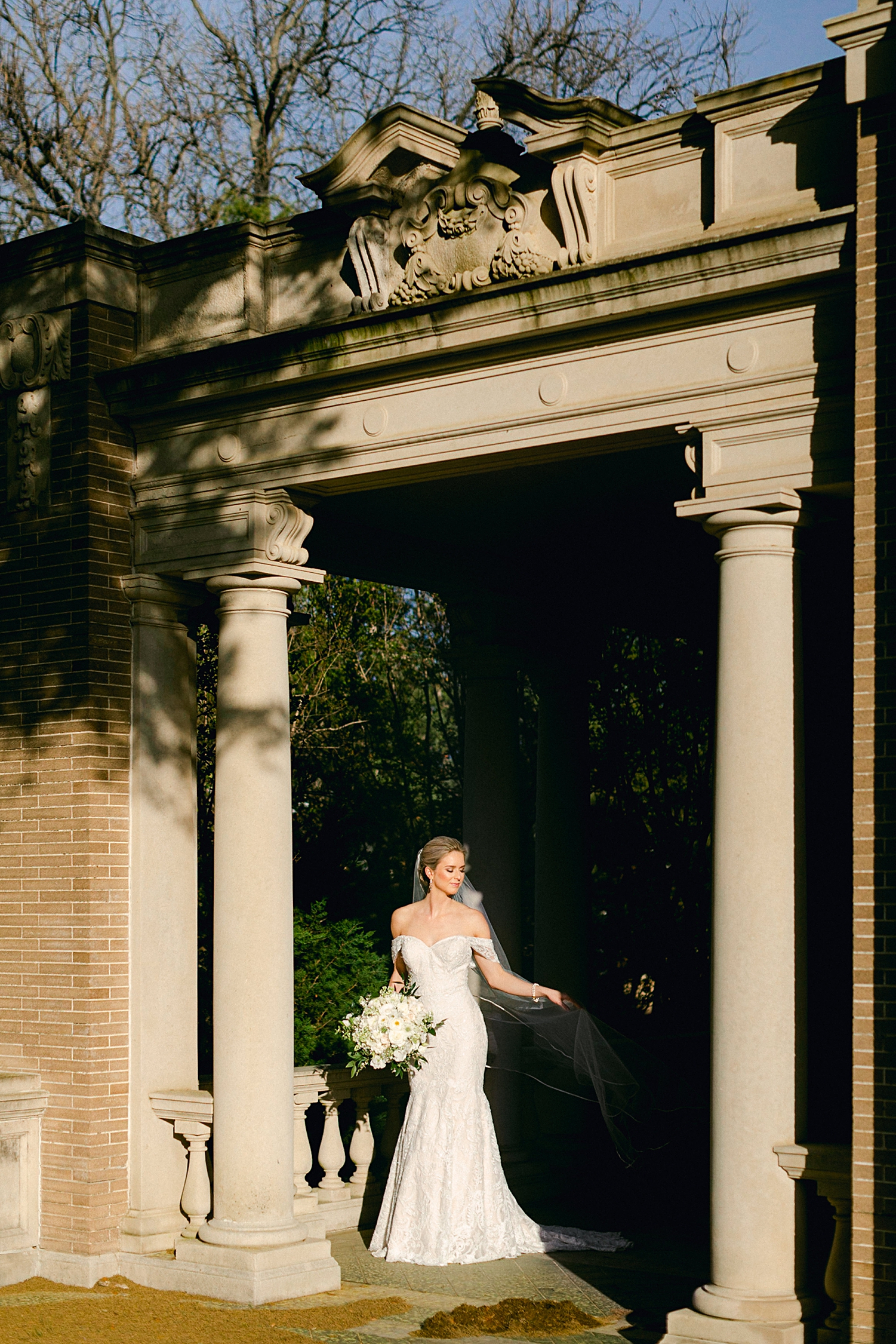 bride in lace wedding dress holding white floral bouquet and laughing between columns bridal session