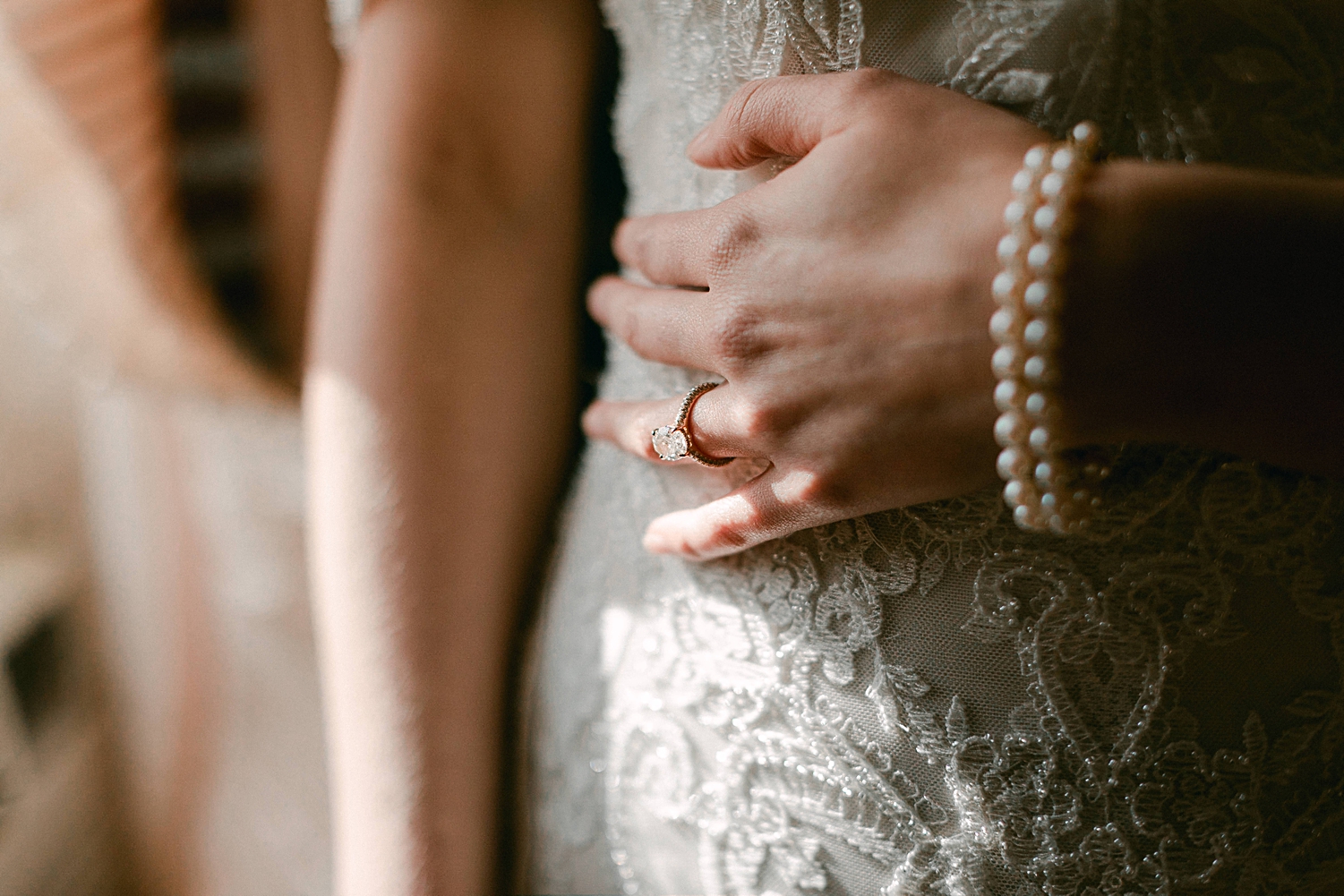 hand with pearl bracelet and engagement ring on lace dress during bridal session