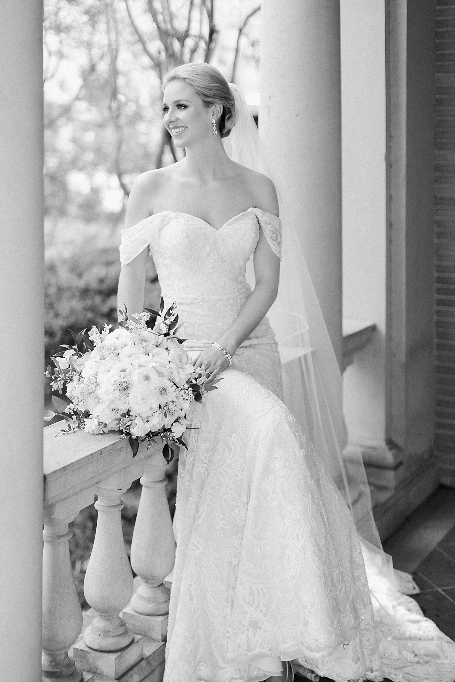 Bride sitting with bouquet in concrete porch columns smiling black and white