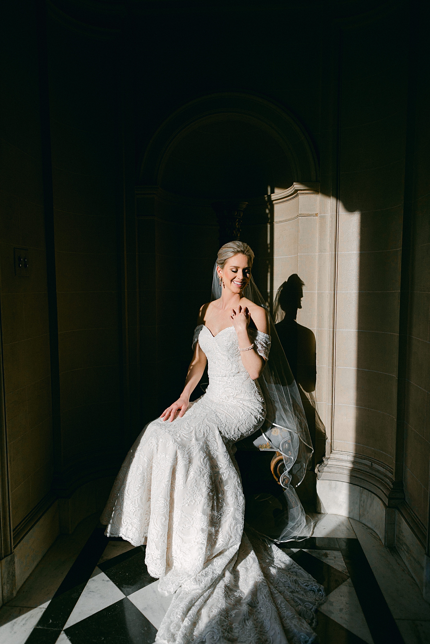 bride in lace wedding dress sitting by stone wall