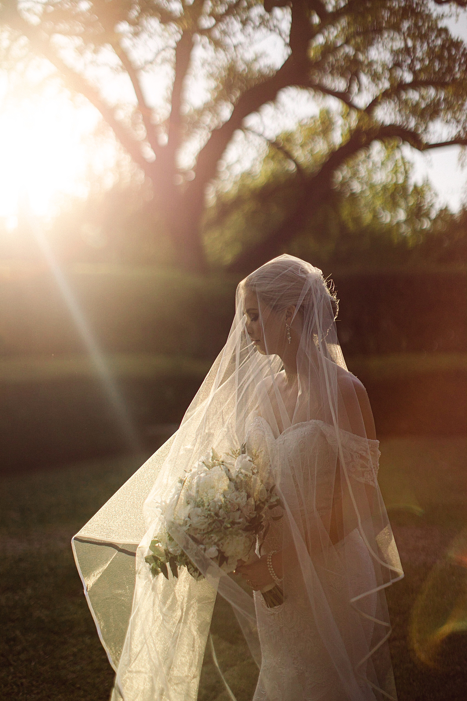 bridal session outdoors bride in wedding dress under veil holding white bouquet at sunset