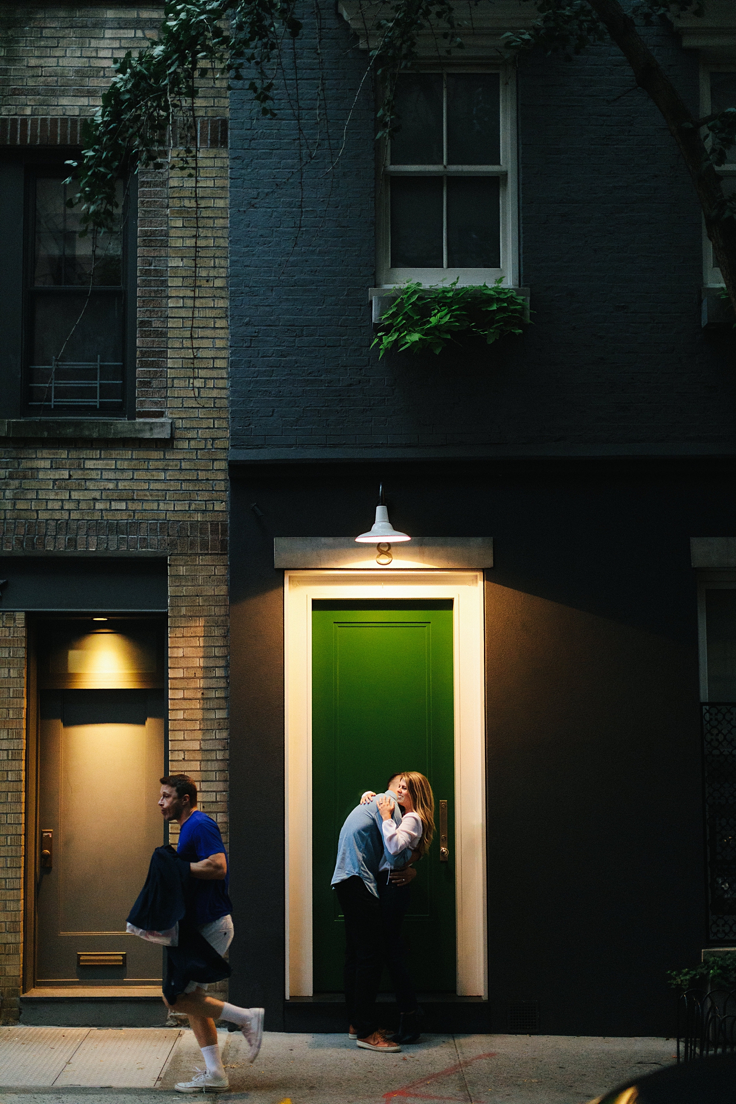 Man and woman embracing in front of green door sidewalk in greenwich city as man runs by