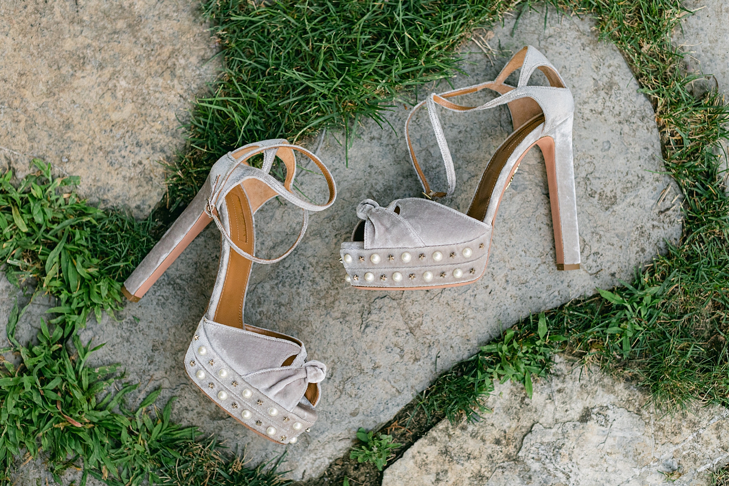 grey high heel bridal shoes laying on stone and green grass 