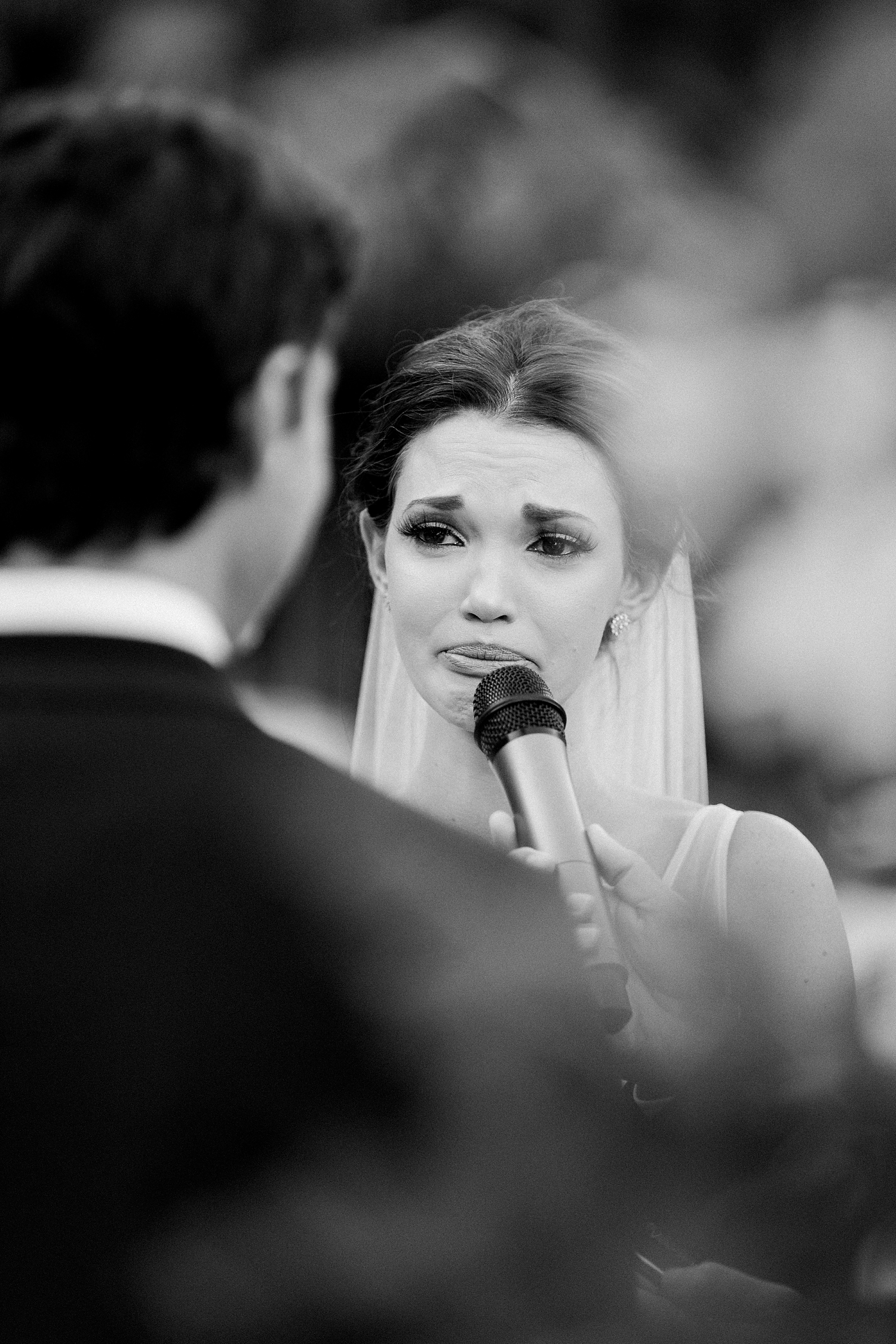 Crying Bride exchanging vows in microphone to groom during wedding ceremony black and white