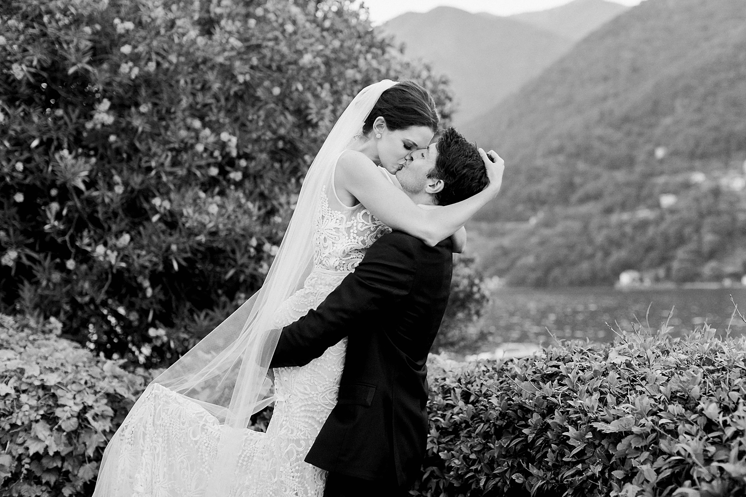 Bride in white lace bridal dress and veil kissing groom by Lake Como Wedding Italy