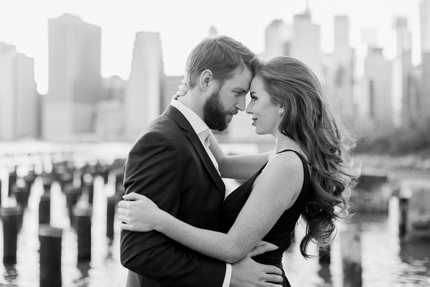 Downtown Manhattan Skyline from Brooklyn pier couple engagement session at sunset touching foreheads in embrace