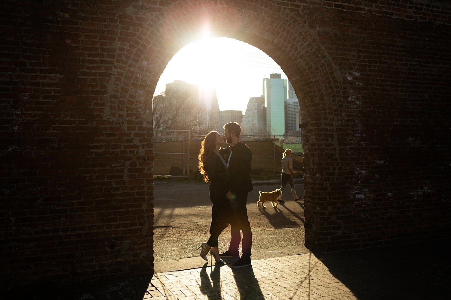 couple standing in archway overlooking downtown manhattan sunset light flare