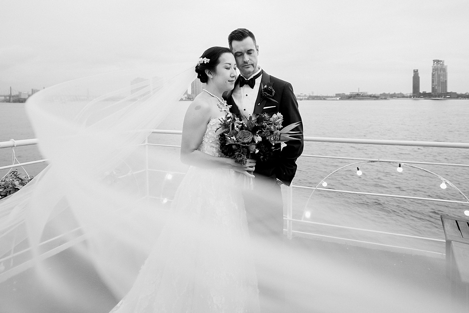 bride and groom standing together at water club in front of east river new york city veil