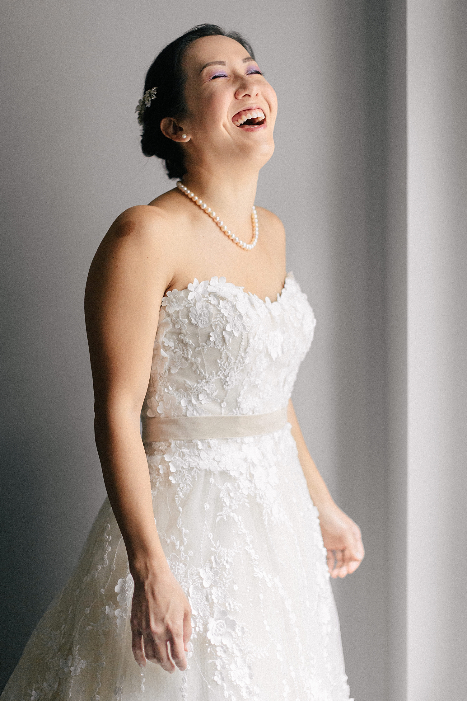 bride in strapless wedding dress pearl necklace laughing