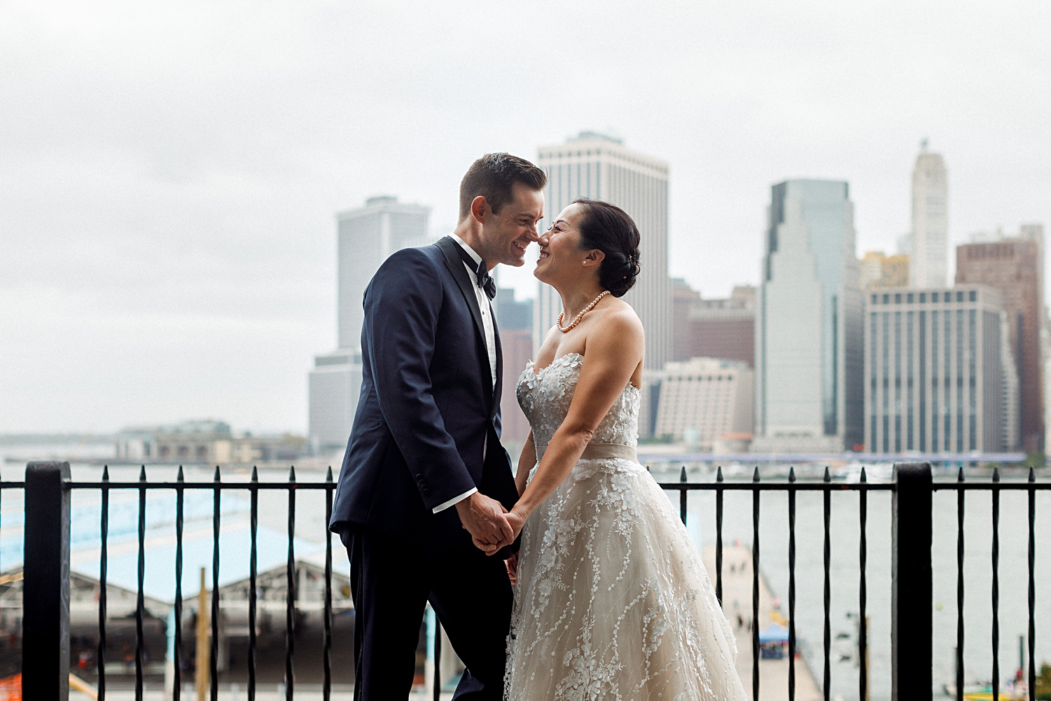 wedding couple standing in front of downtown manhattan skyline from Brooklyn on cloudy day