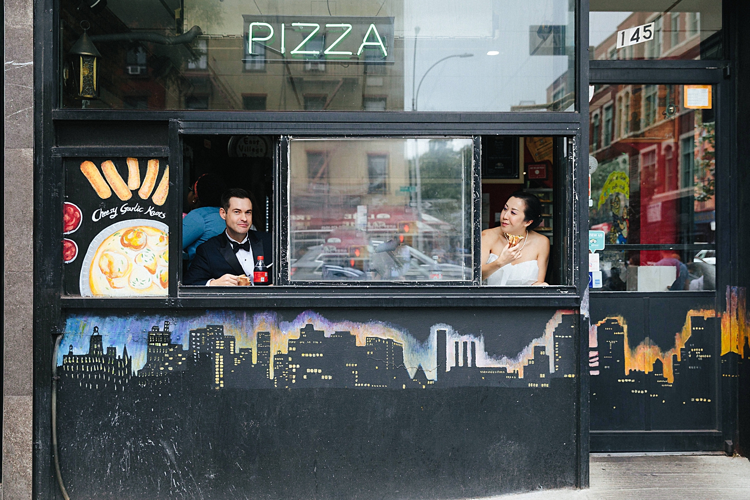 bride and groom eating pizza in new york city pizzeria windows from street