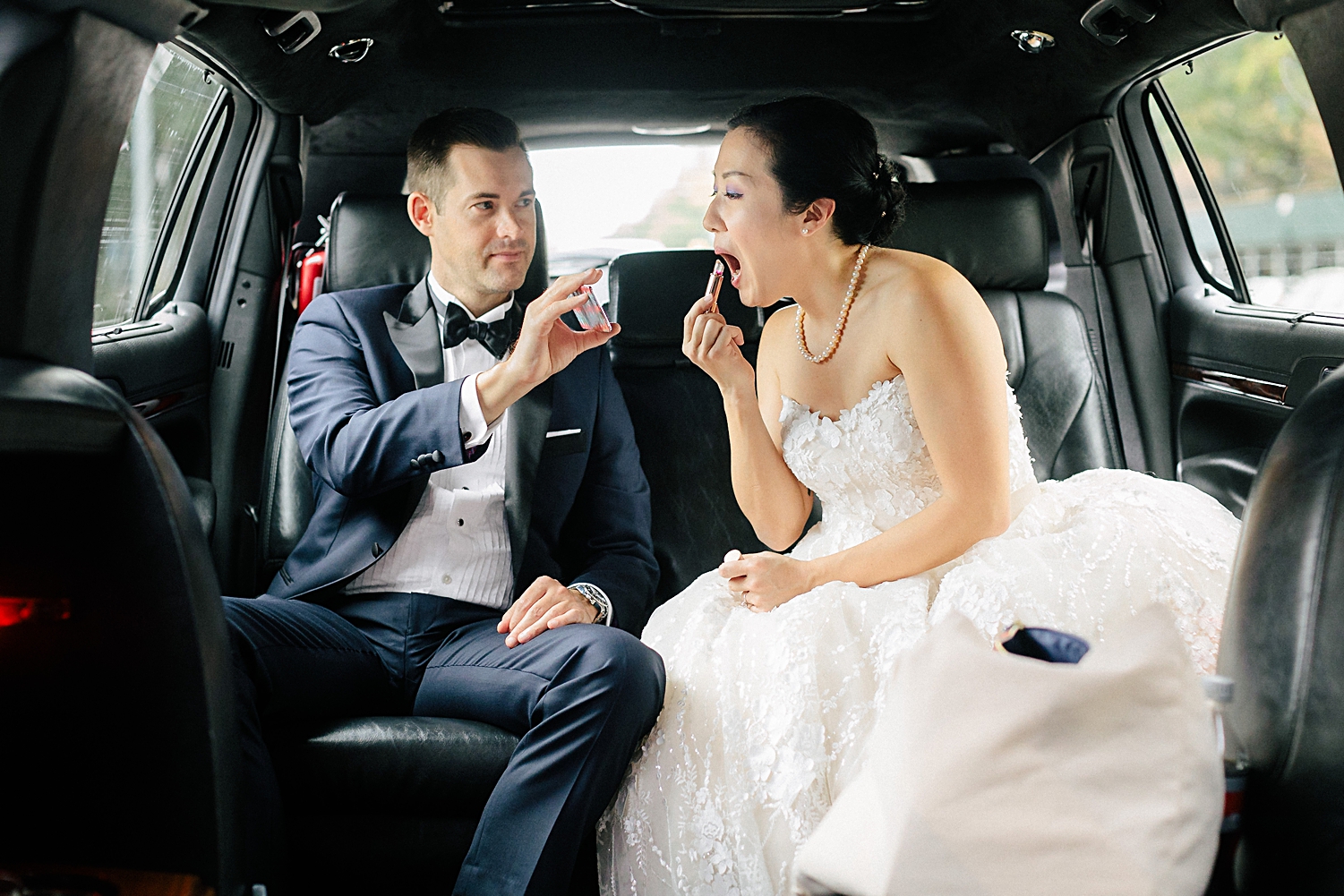 groom holding mirror up for bride to apply lipstick in the back of a limo