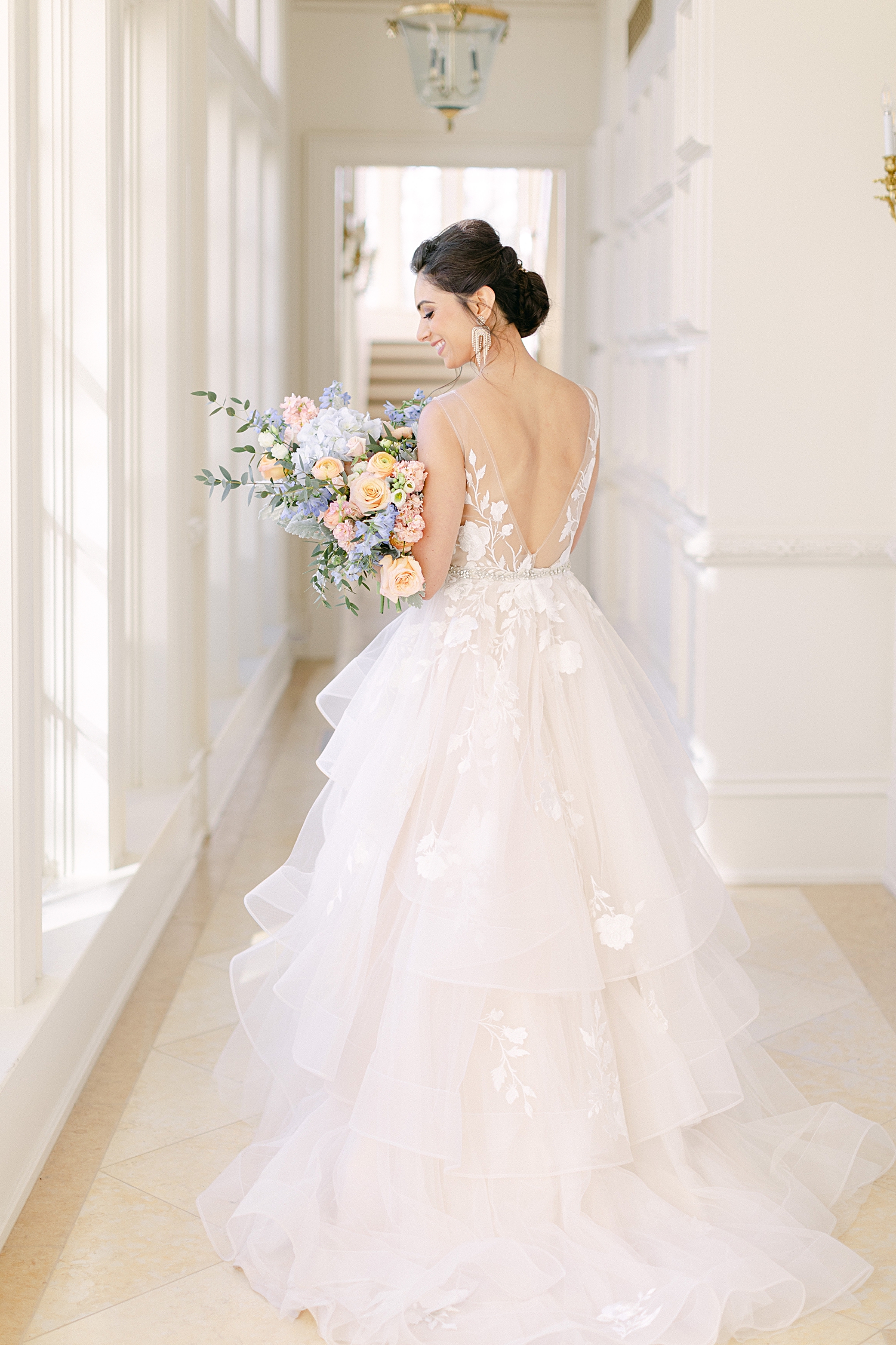 Bride in wedding dress standing in white hallway holding colorful floral bouquet