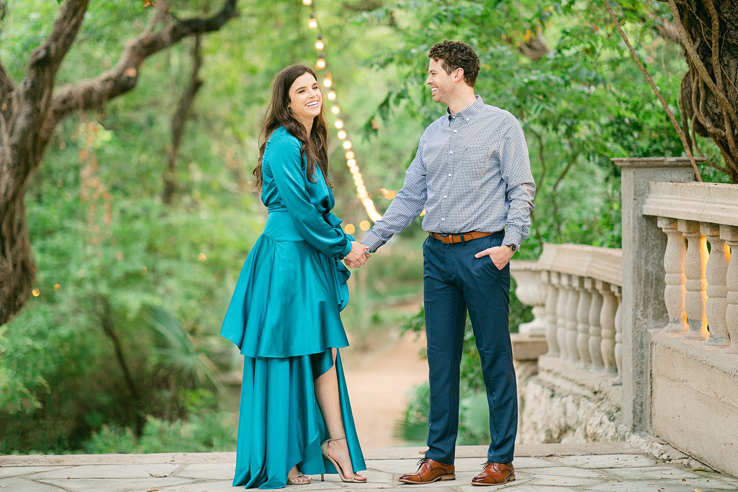 woman in blue dress holding hand with man in front of green trees
