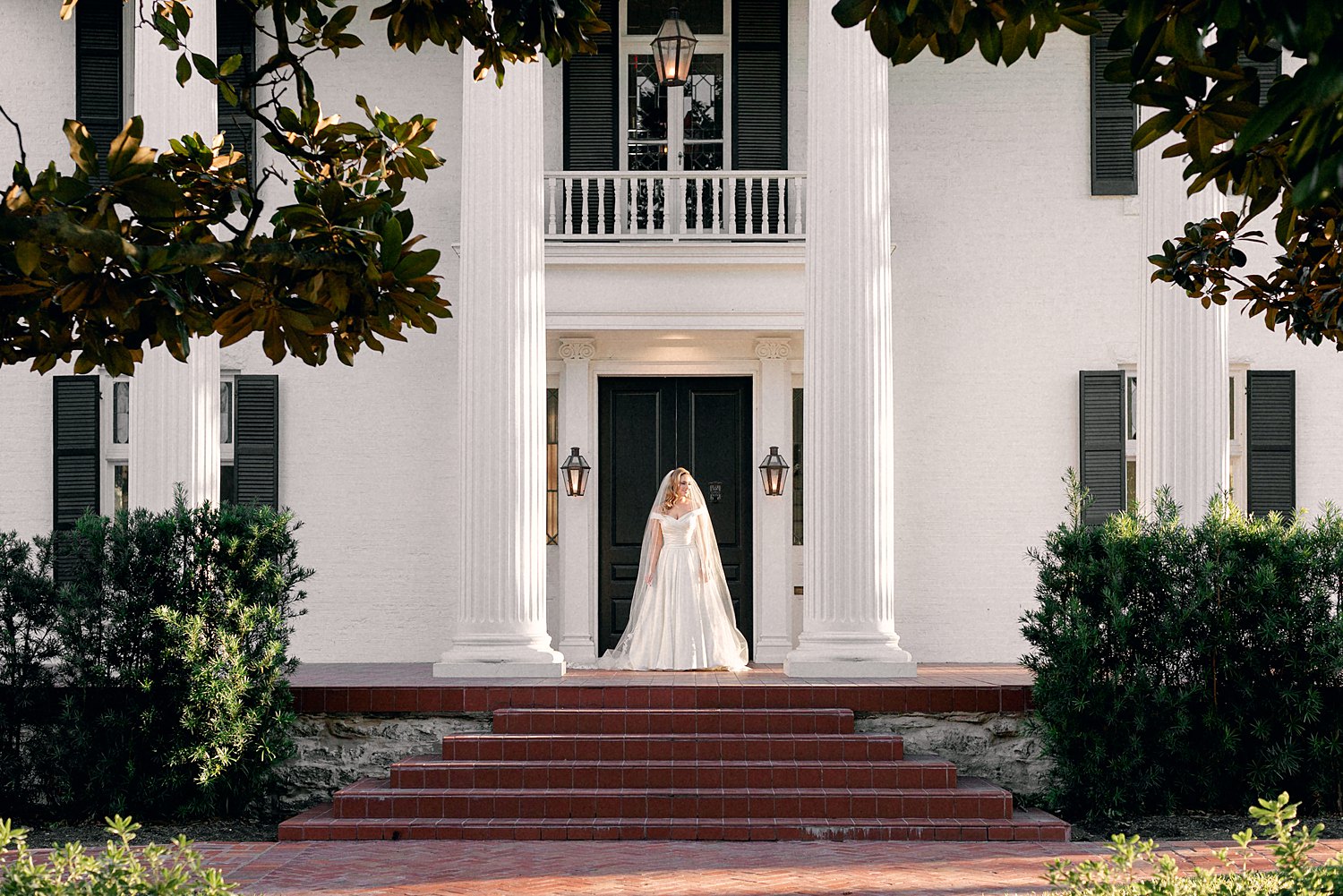 Bride in dress and veil standing on steps of white Woodbine Mansion Austin Wedding Venue