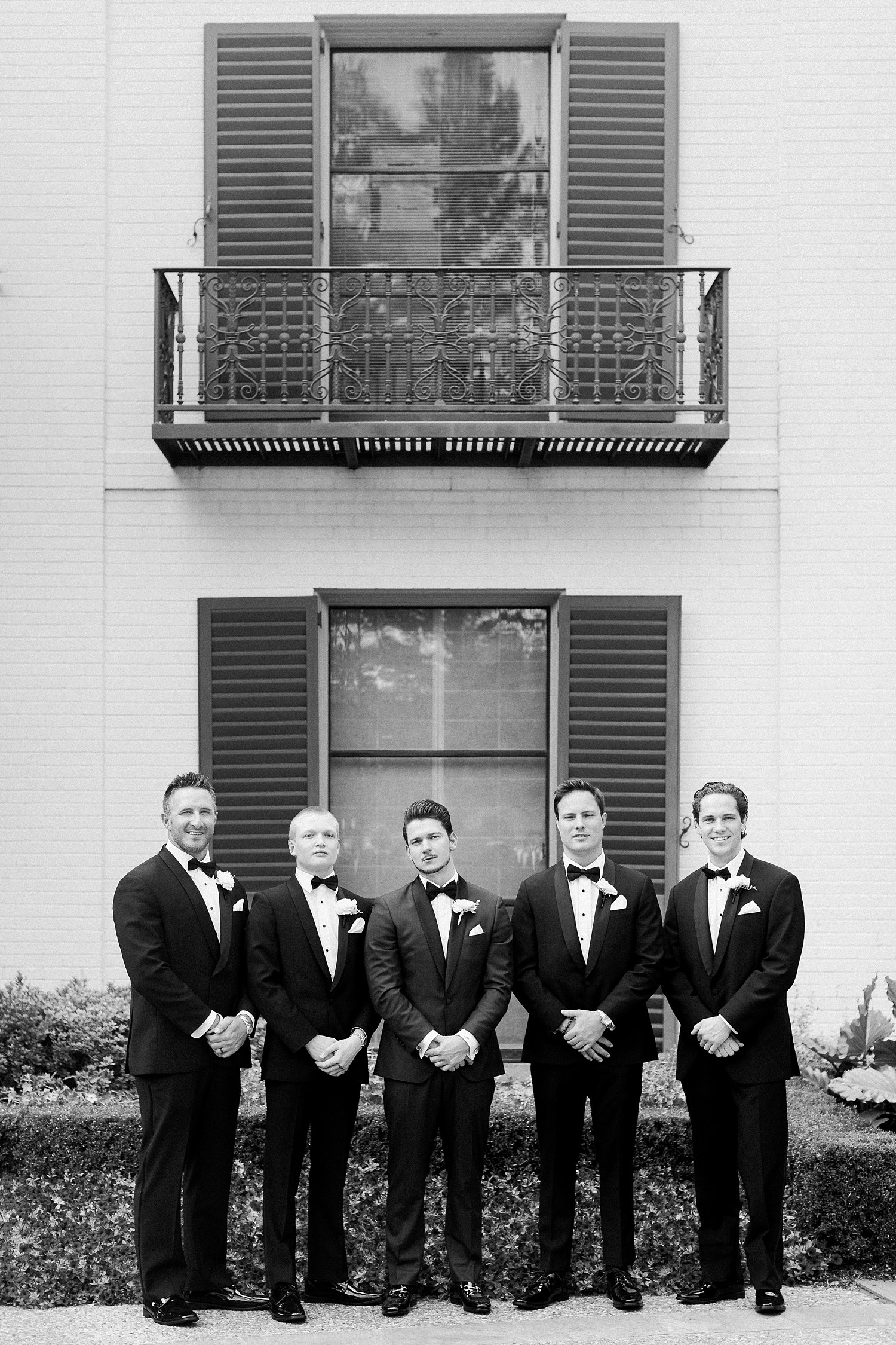 groom and four groomsmen in tuxedos standing in a row in front of white house