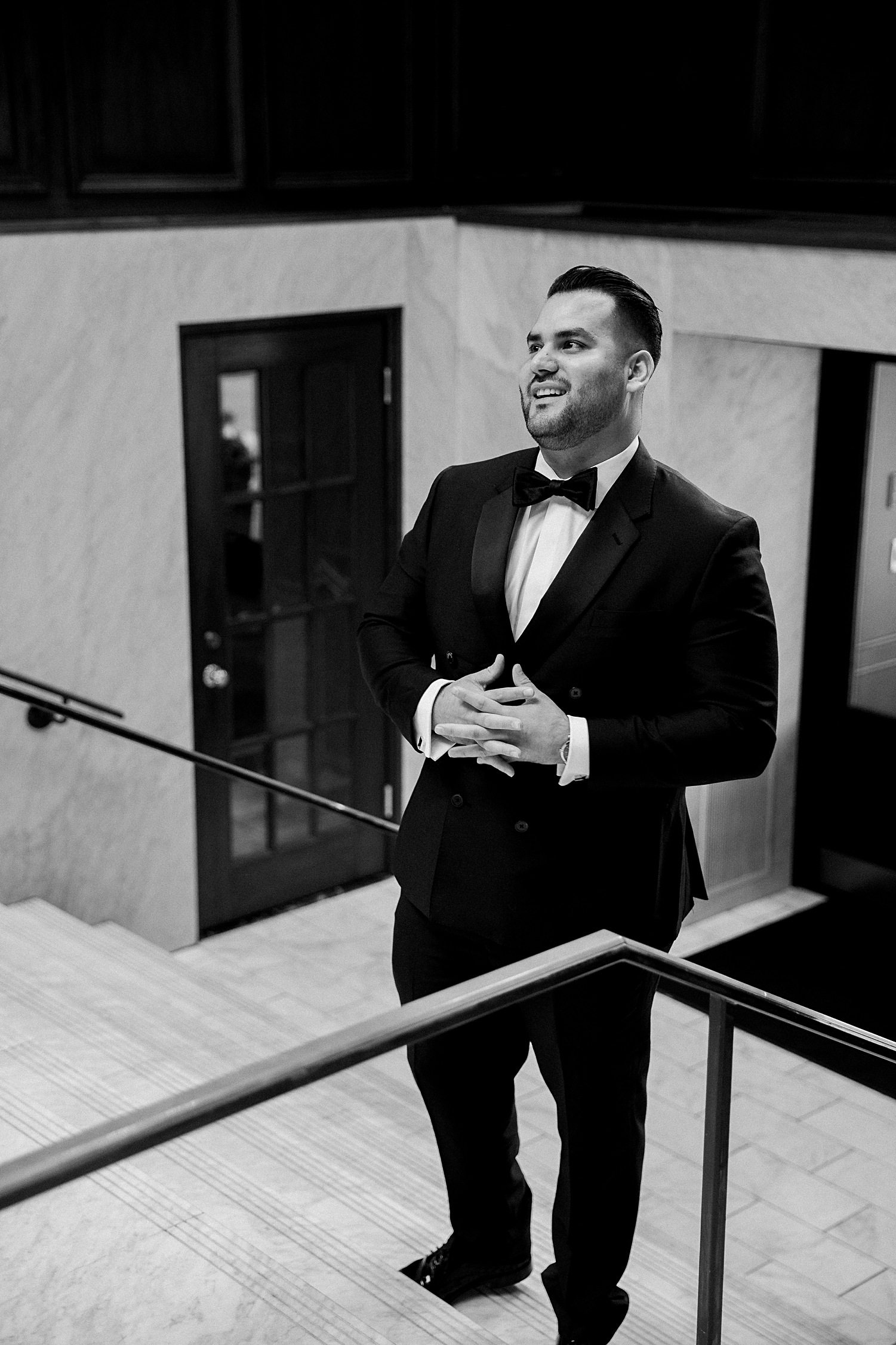 man in black double breasted tuxedo looking up  while standing on stairs 