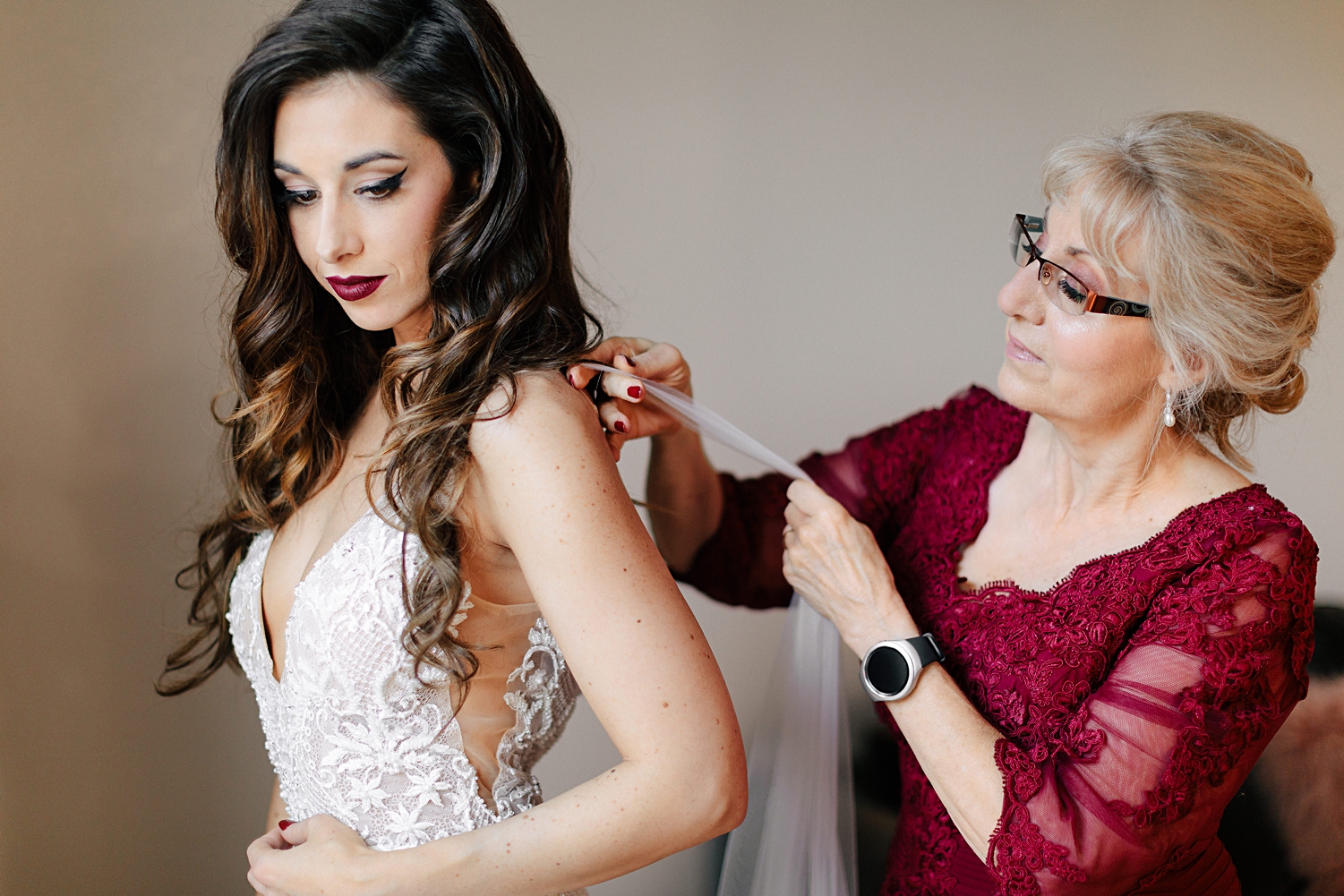 mother in red dress helping bride wedding dress with cape veil