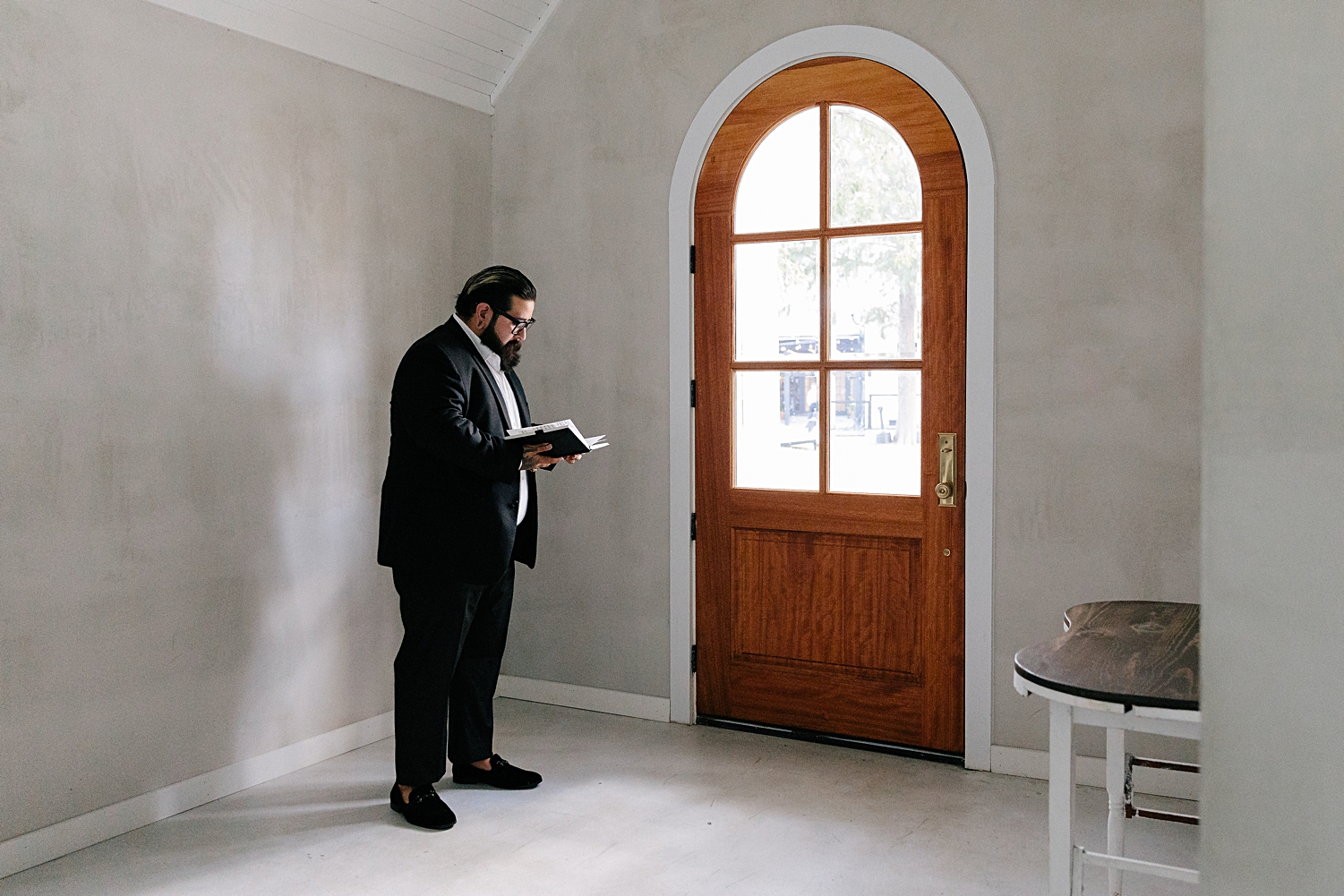 man in black suit reading by window door in white room