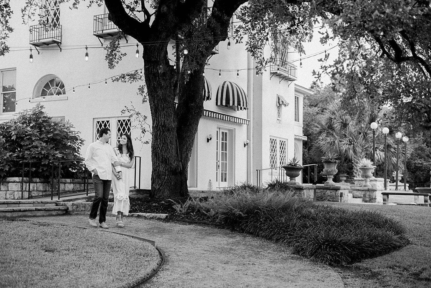 couple walking on path in front of spanish mansion black and white