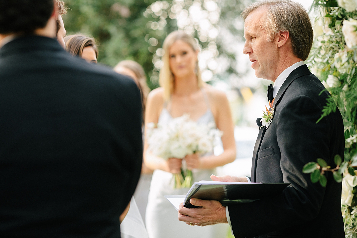 officiant in black suit talking during garden wedding ceremony