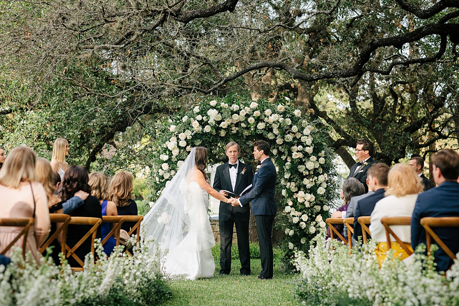 bride and groom at wedding ceremony altar with white floral arch outside Mattie's Austin trees