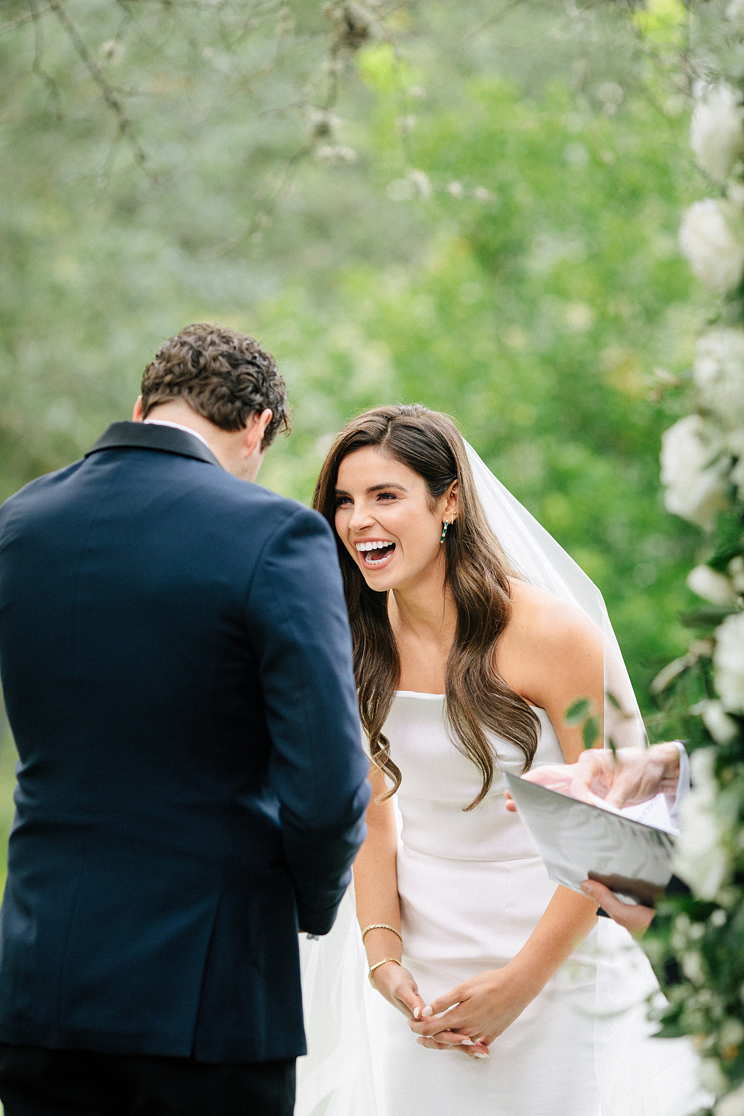 Bride laughing at groom in navy tuxedo at ceremony altar strapless dress