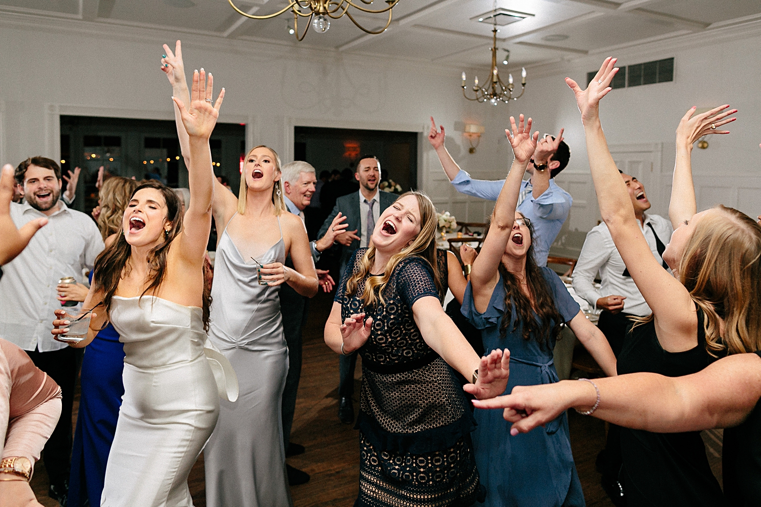 guests singing and dancing with bride at wedding reception white room