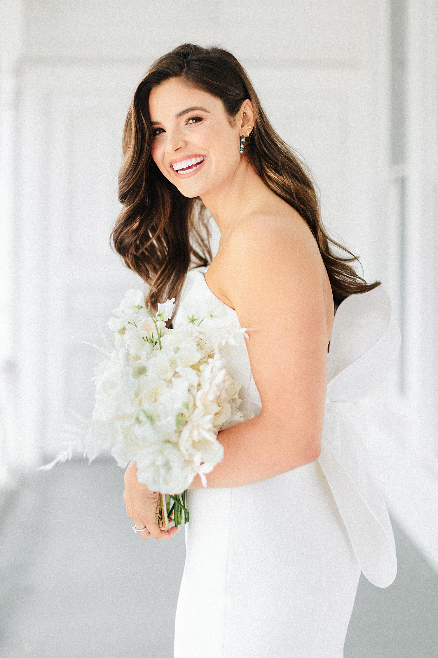 laughing bride in strapless wedding dress with bow standing on white porch with bouquet Mattie's At Green Pastures Austin 
