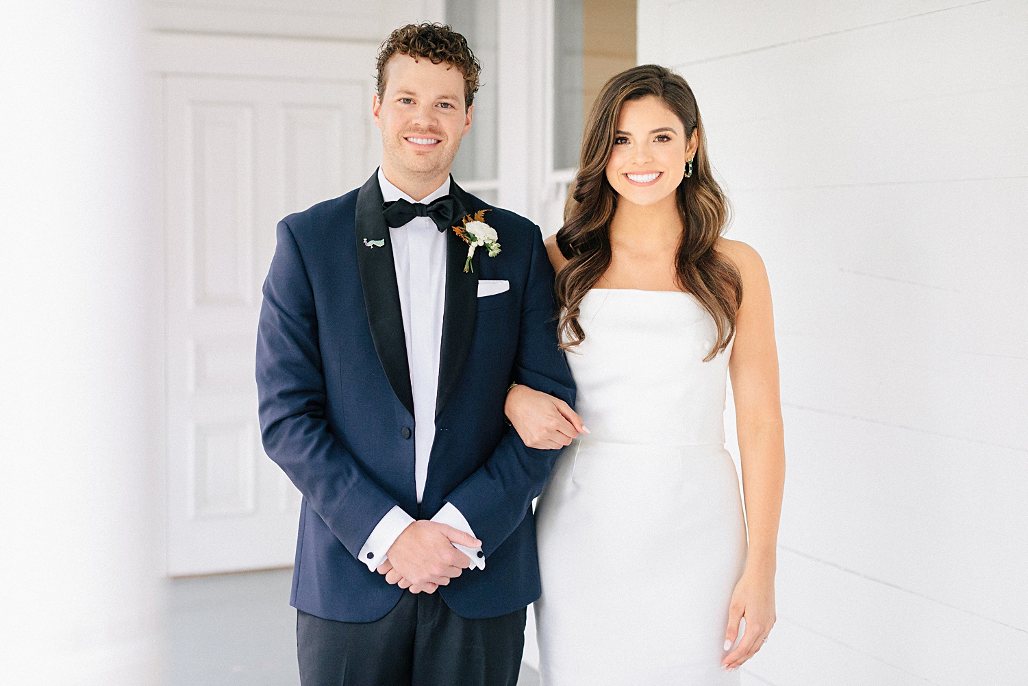 bride in strapless wedding dress with groom in navy tuxedo standing on white porch Mattie's At Green Pastures Austin 